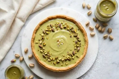 Tarte à la pistache maison avec crème verte et pistaches concassées, vue de dessus sur marbre blanc dans une cuisine artisanale
